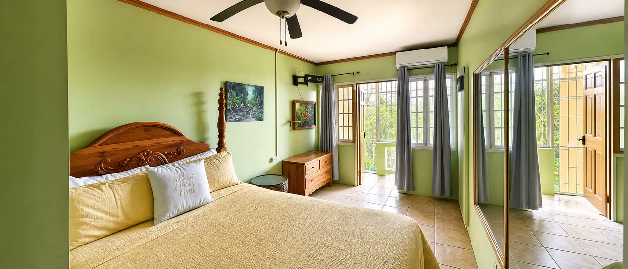 Standard Room interior — carved four-poster bed against soft green walls, French doors open to the hillside
